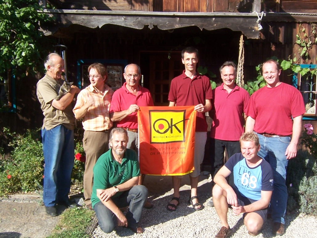 OK-Hafnermeister – die Wurzeln von Original Kachelofen Gruppe der damaligen OK-Hafnermeister mit Original-Kachelofen-Fahne bei einem gemeinsamen Treffen