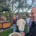 Ein lächelnder Mann hält einen Teller mit Pizza in die Kamera, während sich im Garten mehrere Besucher unterhalten.
